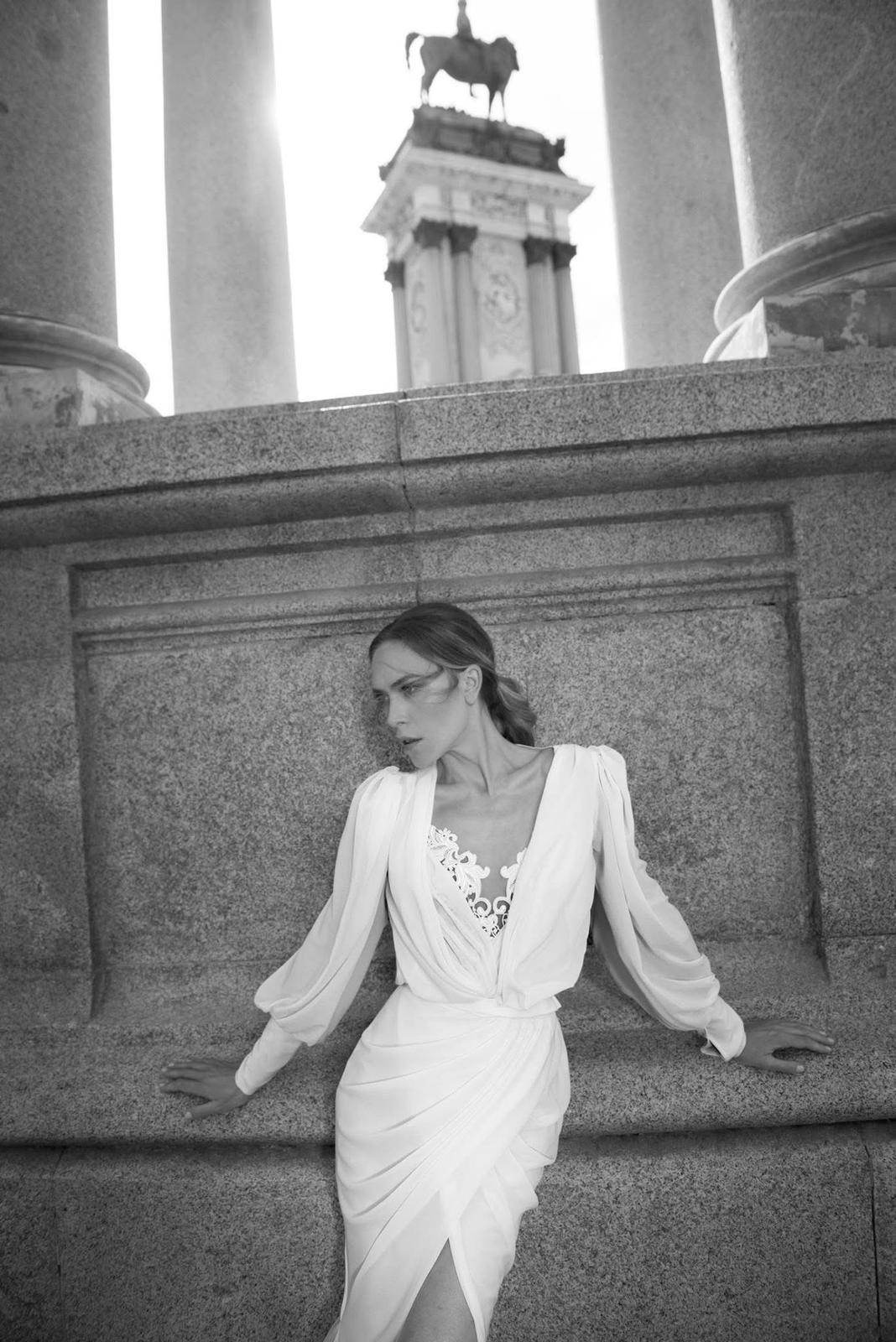 Bride among stone columns, draped-sleeve gown